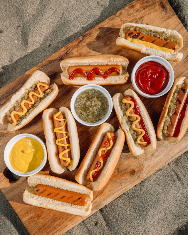 Several hot dogs on a cutting board with different toppings.